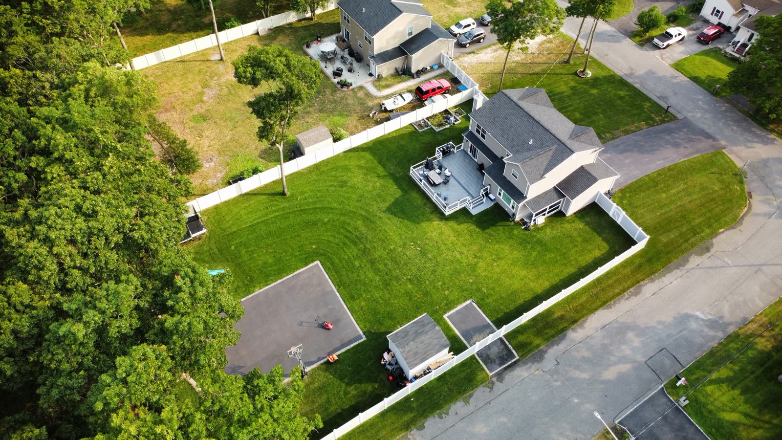 Aerial photo of a two-story home with a deck, fenced backyard and basketball court